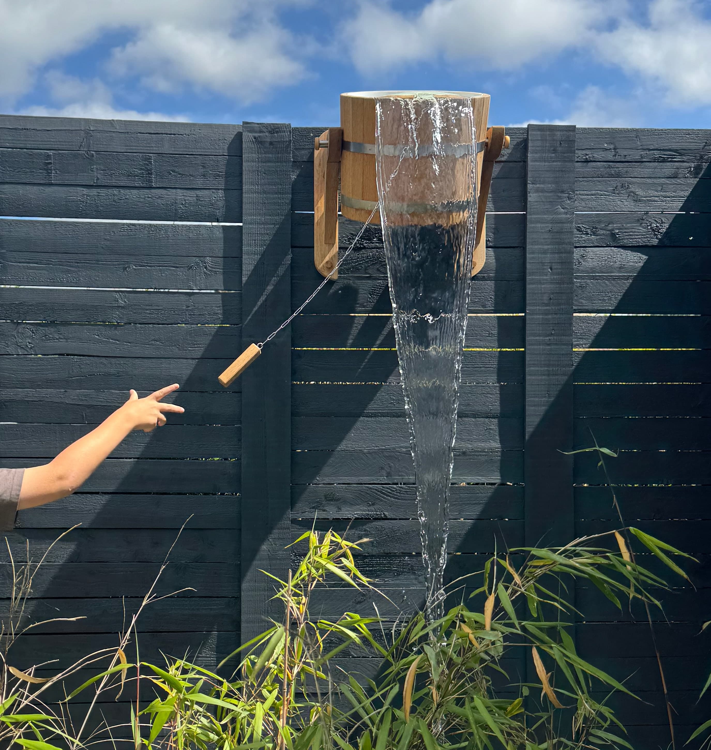 Cold water tipping from the cedar bucket shower down the dark timber cladding