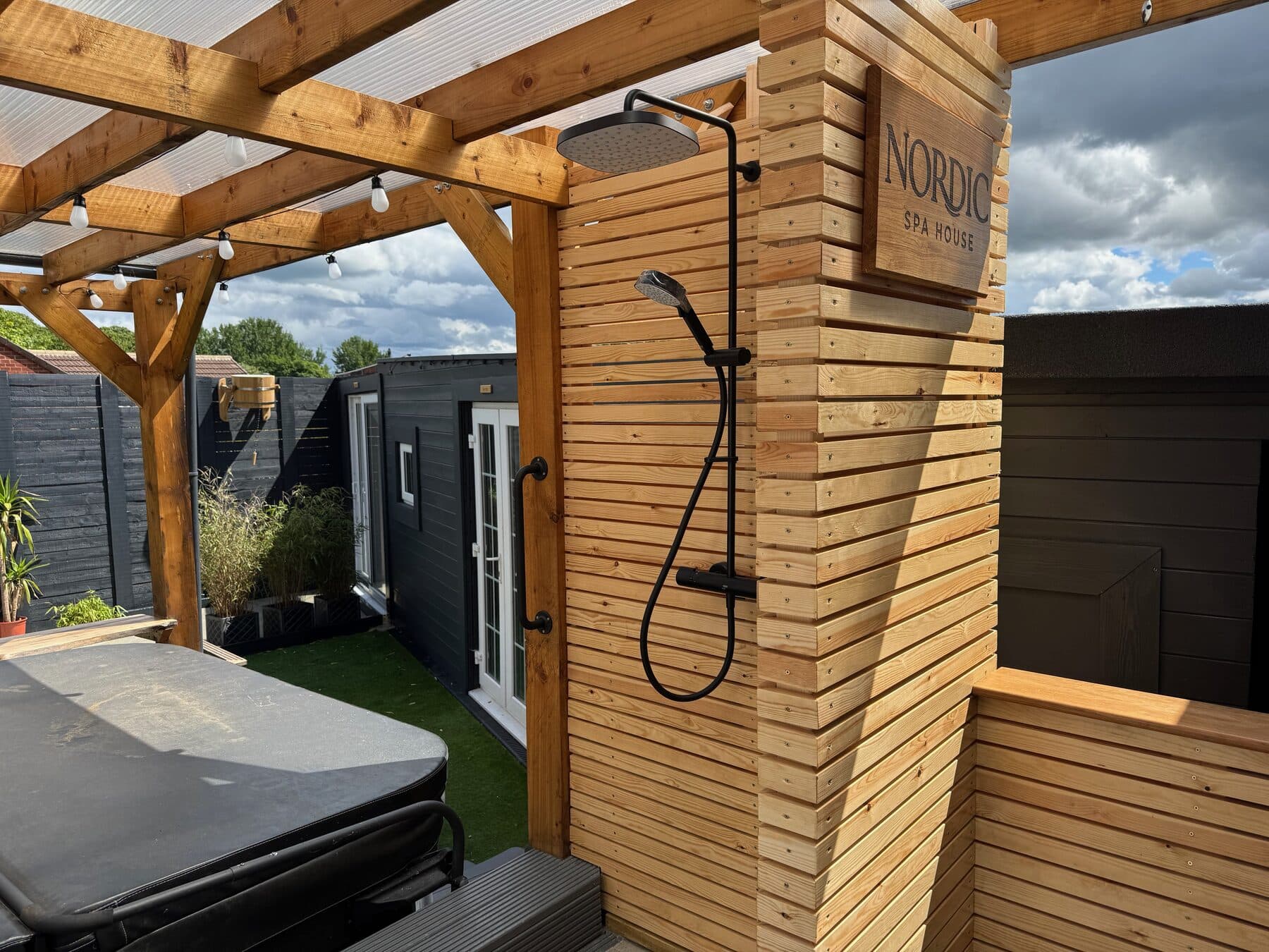 Cedar-clad outdoor rainfall shower beside the hot tub under the pergola